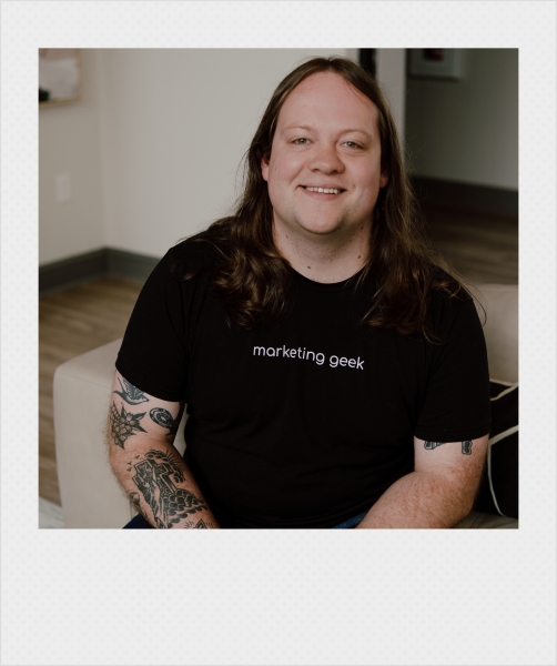 Johnathan Cleghorn, an SEO/SEM manager in Little Rock, Arkansas, sitting and smiling while wearing a black shirt with "marketing geek" written on it. Polaroid-style frame.