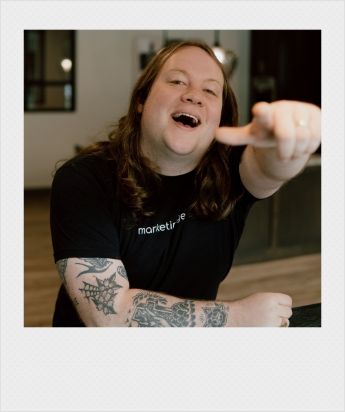 Johnathan Cleghorn, an SEO/SEM manager in Little Rock, Arkansas, laughing and pointing at the camera while wearing a black shirt with "marketing geek" written on it. Polaroid-style frame.