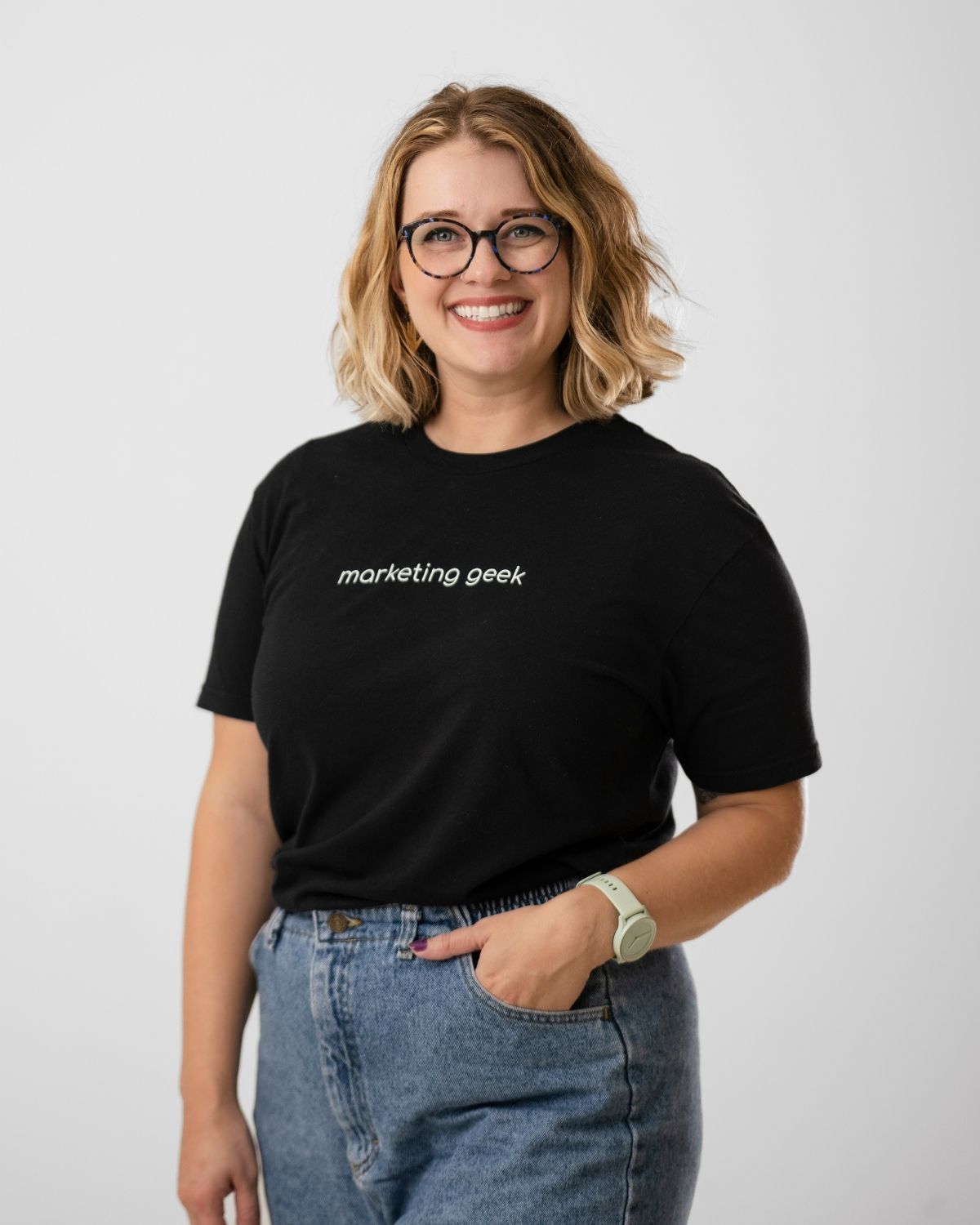 Adrienne Adrienne, senior web designer, stands smiling brightly, wearing "marketing geek" on her black t-shirt, representing the Rock City Digital brand proudly.