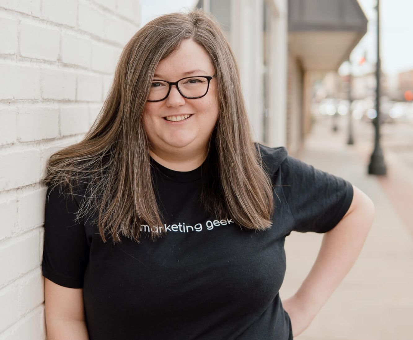 Kenzie Cundall Happiness Geek, stands proudly smiling in a black marketing geek t-shirt.