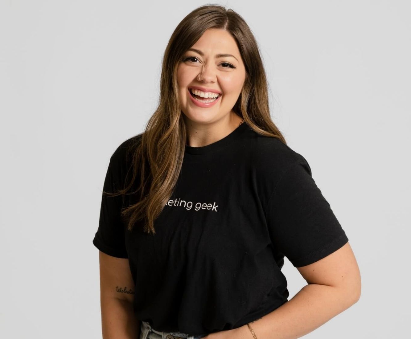 Kenzie Cundall Happiness Geek, stands proudly smiling in a black marketing geek t-shirt.