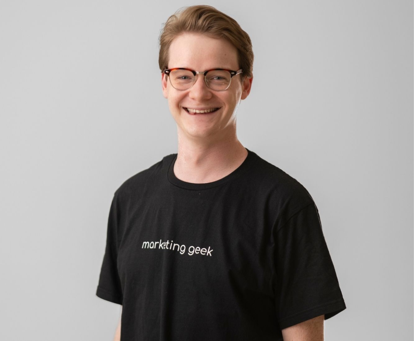 Kenzie Cundall Happiness Geek, stands proudly smiling in a black marketing geek t-shirt.