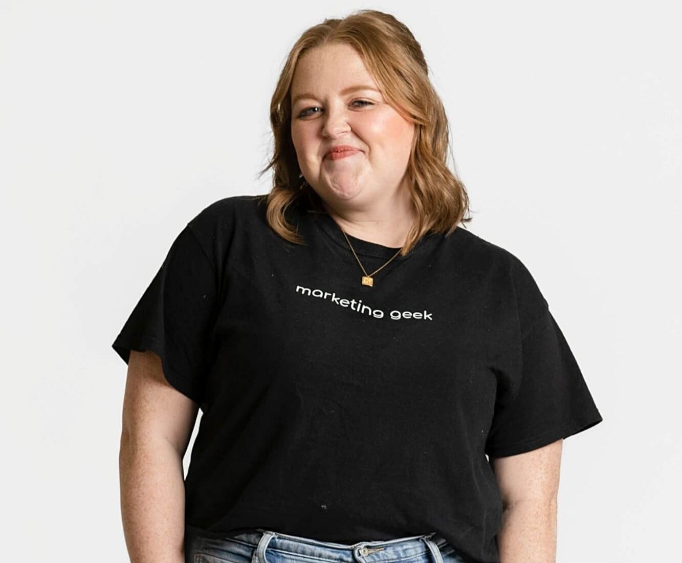 Kenzie Cundall Happiness Geek, stands proudly smiling in a black marketing geek t-shirt.