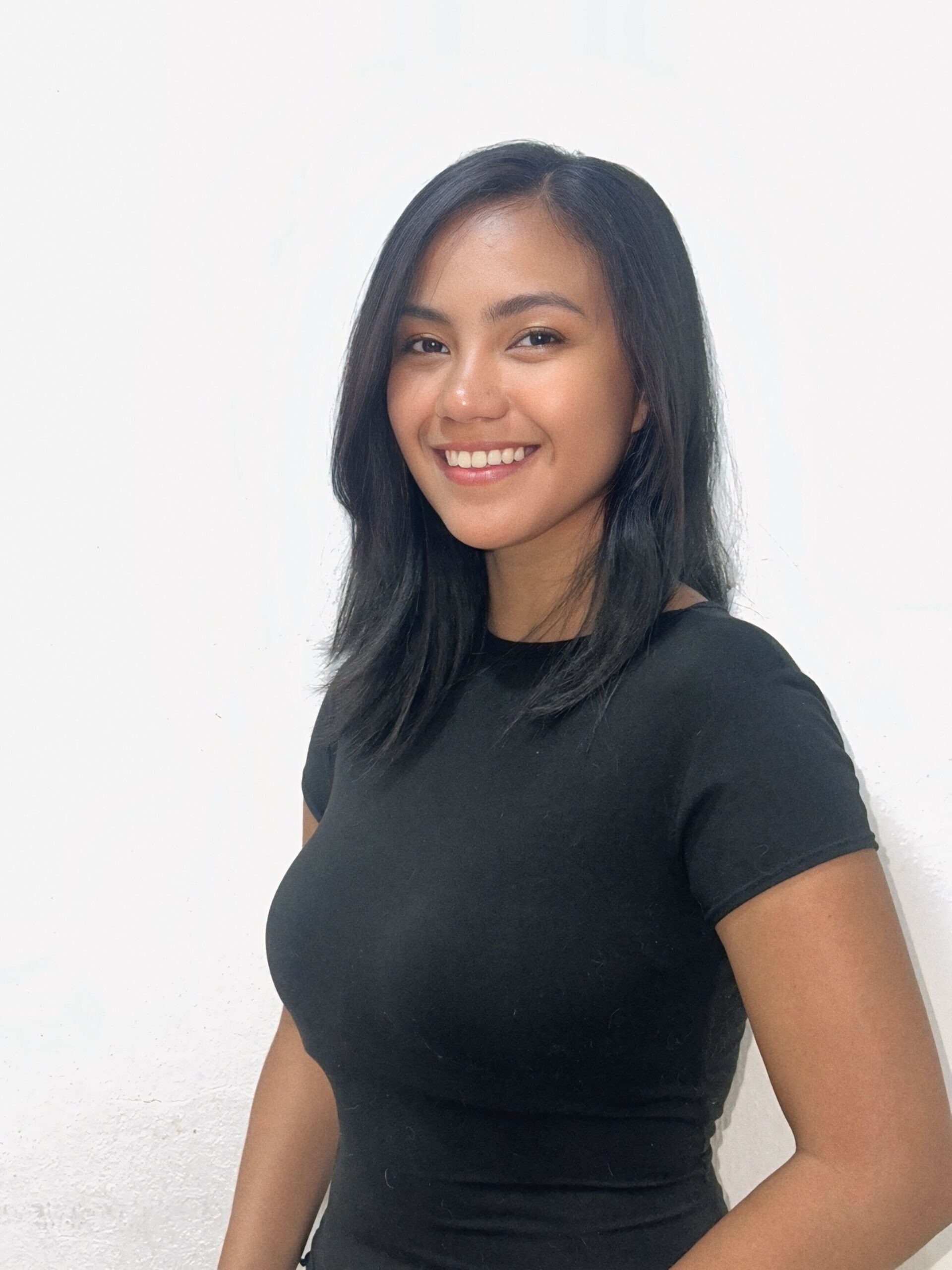 IMG_0789 (1) Abby Pangue with straight, medium-length black hair is smiling at the camera. She is wearing a fitted black t-shirt and standing against a plain white background.