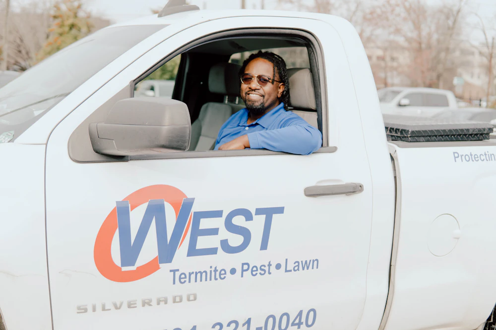 Four men in blue shirts stand beside a white truck, smiling and engaged in conversation outdoors.