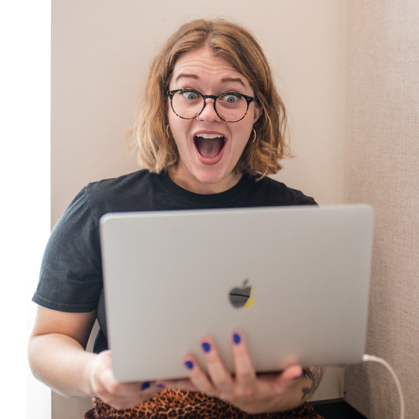 Sarah, account executive, and Kenzie, happiness geek, share a moment laughing together, showcasing camaraderie in their matching marketing geek black t-shirts.